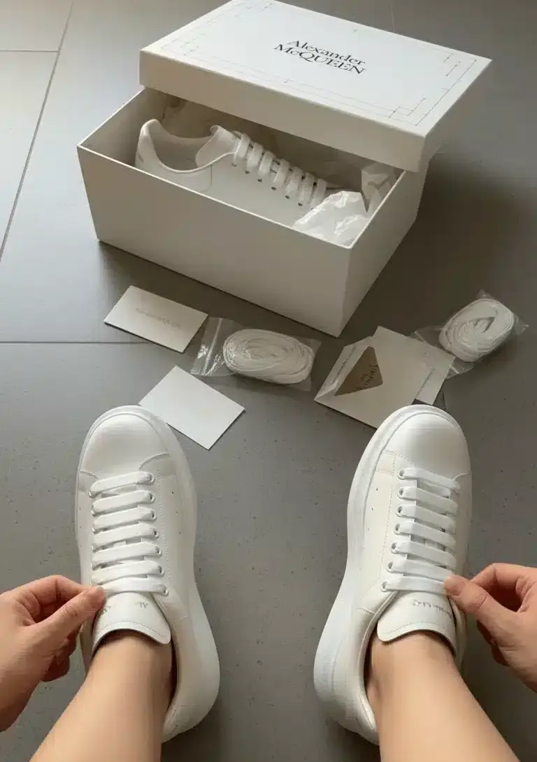 Person unboxing Alexander McQueen Oversized White sneakers with original branded box and accessories – SHUZAR Egypt